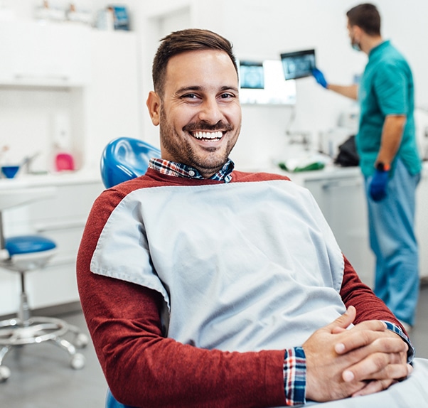 Smiling male patient in dental bib at Smile Santa Fe Dentistry clinic with dentist and assistant in background.