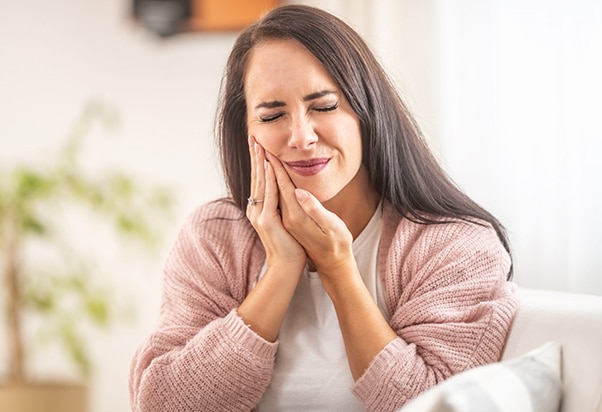 Woman holding her cheek in pain at home, suggesting dental discomfort or toothache.