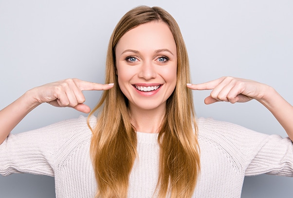 Happy woman pointing to her smile against gray background for dental practice.