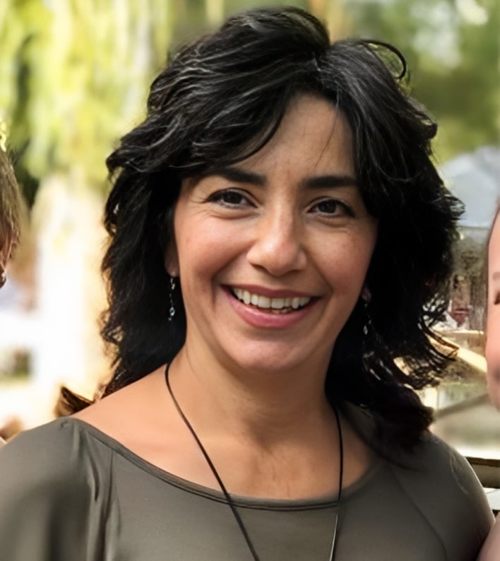 Smiling woman with dark wavy hair outdoors in natural daylight setting.